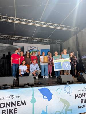 Menschen auf einer Bühne halten einen Pokal und eine Urkunde